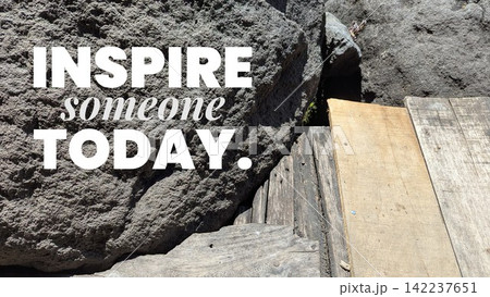 A close up shot shows inspirational motivational quote text stating "INSPIRE someone TODAY." overlaid on a large grey rough stone boulder beside wooden planks. This visual graphic offers a positive A close up shot shows inspirational motivational quote text stating "INSPIRE someone TODAY." overlaid on a large grey rough stone boulder beside wooden planks. This visual graphic offers a positive 142237651