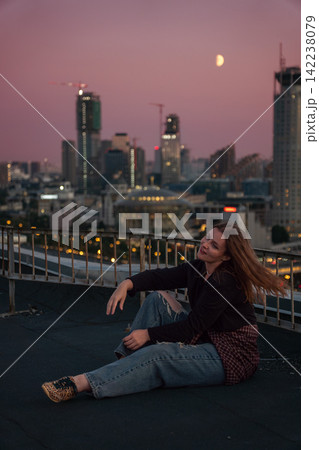 Woman sits on rooftop above Zamoskvorechye district with Moscow skyline and moon at sunset. Travel, urban lifestyle, city exploration, rooftop leisure, tourism, freedom. Woman sits on rooftop above Zamoskvorechye district with Moscow skyline and moon at sunset. Travel, urban lifestyle, city exploration, rooftop leisure, tourism, freedom. 142238079