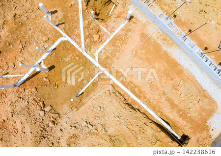 Workers are laying white pipes in fresh dirt at construction site under building foundation, Workers are laying white pipes in fresh dirt at construction site under building foundation, 142238616