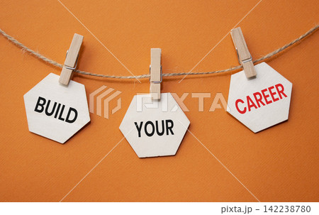 Build Your Career text on wooden hexagon tags hanging on rope with clothespins over orange background. Professional growth and career development concept with copy space. 142238780