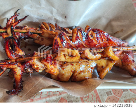 Freshly grilled and smoked squid skewers served on paper wrapping at a local street food market stall in Trenggalek, East Java. Freshly grilled and smoked squid skewers served on paper wrapping at a local street food market stall in Trenggalek, East Java. 142239039