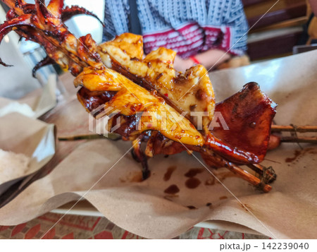 Freshly grilled and smoked squid skewers served on paper wrapping at a local street food market stall in Trenggalek, East Java. Freshly grilled and smoked squid skewers served on paper wrapping at a local street food market stall in Trenggalek, East Java. 142239040