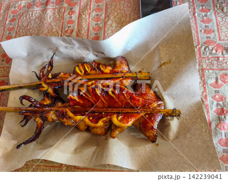 Freshly grilled and smoked squid skewers served on paper wrapping at a local street food market stall in Trenggalek, East Java. Freshly grilled and smoked squid skewers served on paper wrapping at a local street food market stall in Trenggalek, East Java. 142239041