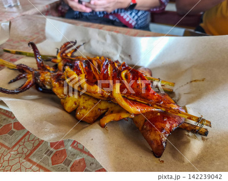 Freshly grilled and smoked squid skewers served on paper wrapping at a local street food market stall in Trenggalek, East Java. 142239042