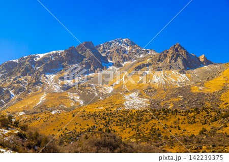 Rugged Mountain Range with Snow Patches Under Blue Sky Rugged Mountain Range with Snow Patches Under Blue Sky 142239375