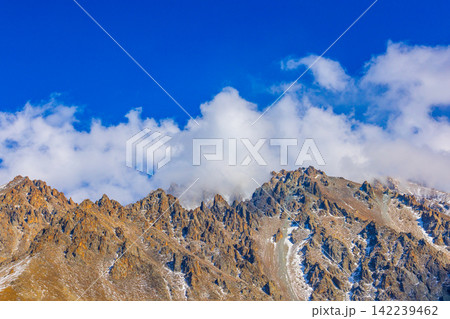 Jagged Mountain Peaks Under Blue Sky with Clouds 142239462