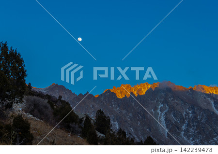Majestic Mountain Range at Sunrise with Full Moon in Kyrgyzstan Majestic Mountain Range at Sunrise with Full Moon in Kyrgyzstan 142239478