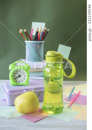 School supplies and healthy lunch on the study table. Bottle of water and lunch box and alarm clock, textbooks, colored pencils: back to school concept. 142239546