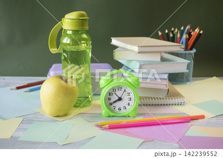 School supplies and healthy lunch on the study table. Bottle of water and lunch box and alarm clock, textbooks, colored pencils: back to school concept. School supplies and healthy lunch on the study table. Bottle of water and lunch box and alarm clock, textbooks, colored pencils: back to school concept. 142239552