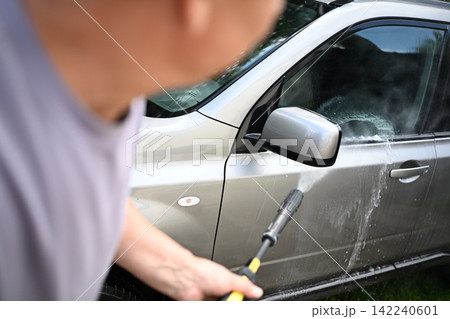 Senior man pressure washing dirty car during outdoor home car wash Senior man pressure washing dirty car during outdoor home car wash 142240601