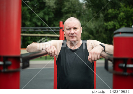 Mature man resting on parallel bars at outdoor gym Mature man resting on parallel bars at outdoor gym 142240622