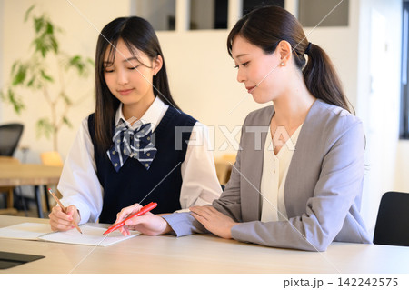 先生が生徒に勉強を教える、個別指導の様子 先生が生徒に勉強を教える、個別指導の様子 142242575