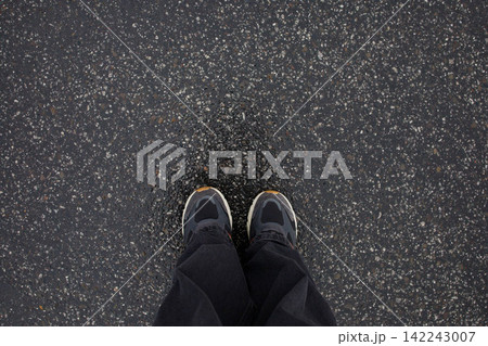 Feet of woman in sneakers and loose grey jeans standing on wet asphalt after the rain close up top view. Human in the city, walk in rainy weather, minimalistic background Feet of woman in sneakers and loose grey jeans standing on wet asphalt after the rain close up top view. Human in the city, walk in rainy weather, minimalistic background 142243007