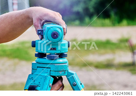 Surveyor steadies optical instrument by hand while setting tripod mounted level for accurate construction layout and land measurement tasks. 142243061