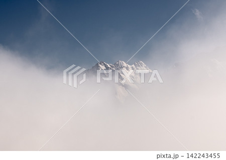 Snow covered mountain peaks emerging through thick white clouds Snow covered mountain peaks emerging through thick white clouds 142243455