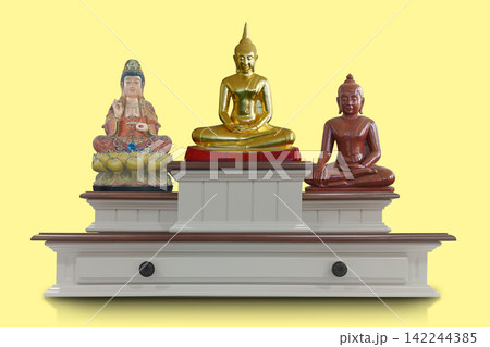 front view features three distinct sacred statues displayed on a tiered, white wood altar stand against a solid pale yellow background, religion, buddha, copy space front view features three distinct sacred statues displayed on a tiered, white wood altar stand against a solid pale yellow background, religion, buddha, copy space 142244385
