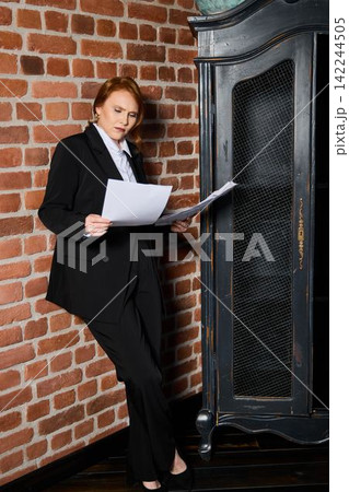 Professional woman carefully proofreading antique cabinet setting Professional woman carefully proofreading antique cabinet setting 142244505