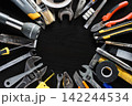 Assorted hand tools and repair supplies arranged around empty center on dark workshop surface 142244534