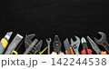 Assorted worn hand tools arranged along bottom edge on dark scratched work surface with wide copy space above 142244538