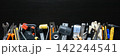 Assorted hand tools, paint brush, gloves, utility knives, pliers, wrench, tape, rulers and hammer arranged in row on black background for repair 142244541