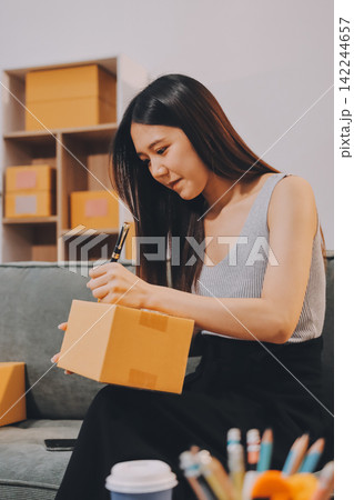 Startup SME small business entrepreneur of freelance Asian woman wearing apron using laptop and box to receive and review orders online to prepare to pack sell to customers, online sme business ideas. Startup SME small business entrepreneur of freelance Asian woman wearing apron using laptop and box to receive and review orders online to prepare to pack sell to customers, online sme business ideas. 142244657