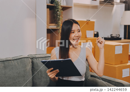 Startup SME small business entrepreneur of freelance Asian woman wearing apron using laptop and box to receive and review orders online to prepare to pack sell to customers, online sme business ideas. Startup SME small business entrepreneur of freelance Asian woman wearing apron using laptop and box to receive and review orders online to prepare to pack sell to customers, online sme business ideas. 142244659
