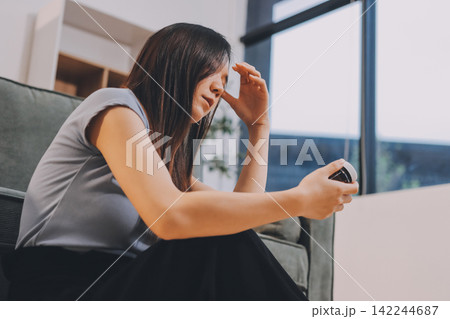 Young Asian woman sitting in bed and holding her head in pain with headache, feeling depressed and suffering 142244687