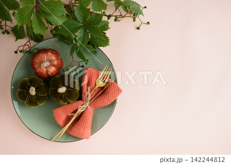 Elegant Thanksgiving table setting with decorative pumpkins, golden cutlery, and autumnal foliage on a pastel background 142244812