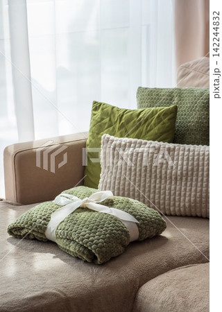 Cozy green blanket tied with white ribbon resting on comfortable sofa with plush pillows Cozy green blanket tied with white ribbon resting on comfortable sofa with plush pillows 142244832