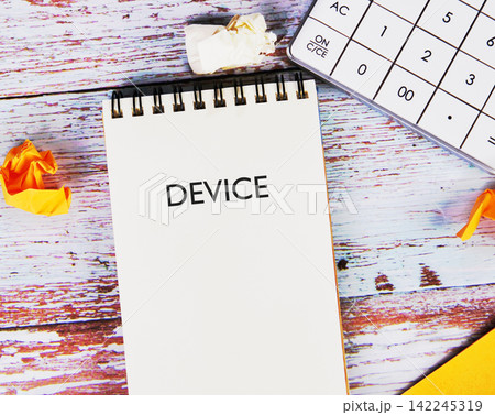 DEVICE word text written on a spiral notepad placed on a wooden desk next to a calculator DEVICE word text written on a spiral notepad placed on a wooden desk next to a calculator 142245319