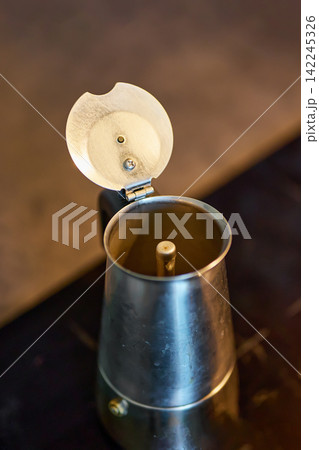 Close up detailed view of an open classic Italian silver moka pot espresso maker standing on a dark modern kitchen stove Close up detailed view of an open classic Italian silver moka pot espresso maker standing on a dark modern kitchen stove 142245326