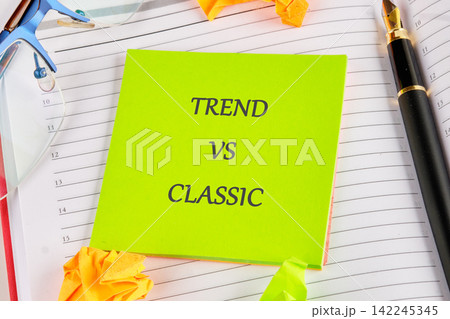 Fashion and marketing concept showing Trend vs Classic text on a bright green sticky note placed over an open planner 142245345