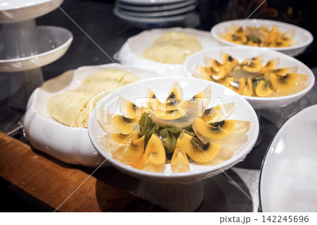 Assorted traditional Asian dishes displayed in white bowls, featuring sliced yellow eggs, noodles, and green vegetables on a wooden table in a restaurant setting 142245696