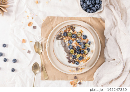 Healthy breakfast bowl with yogurt granola blueberries and chia seeds served in a rustic dish for a nutritious start to the day on white fabric Healthy breakfast bowl with yogurt granola blueberries and chia seeds served in a rustic dish for a nutritious start to the day on white fabric 142247280
