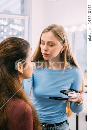 Visage routine. Aesthetic makeup. Female professional cosmetologist applying face skin product using tool in studio workspace. 142248143