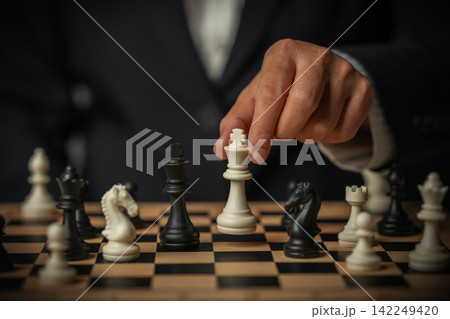 business hand placing white chess king facing off a black on board surrounded by pieces business hand placing white chess king facing off a black on board surrounded by pieces 142249420