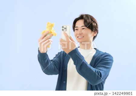 ぬいぐるみをスマートフォンで撮影する若い男性 ぬいぐるみをスマートフォンで撮影する若い男性 142249901