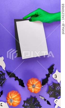 Green witch hand holding blank card mockup over purple Halloween background Green witch hand holding blank card mockup over purple Halloween background 142250468