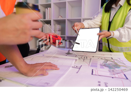 Engineers holding digital tablet mockup and walkie talkie over blueprint for construction planning Engineers holding digital tablet mockup and walkie talkie over blueprint for construction planning 142250469