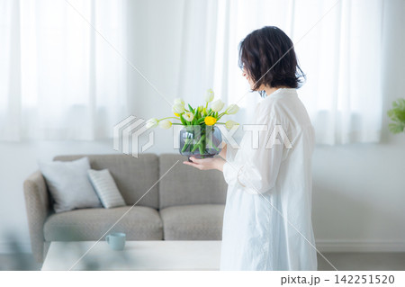 リビングで花瓶を持つる若い女性 リビングで花瓶を持つる若い女性 142251520