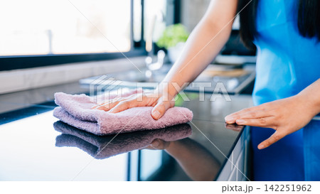 A cheerful housewife ensures safety and hygiene by wiping her kitchen table A cheerful housewife ensures safety and hygiene by wiping her kitchen table 142251962