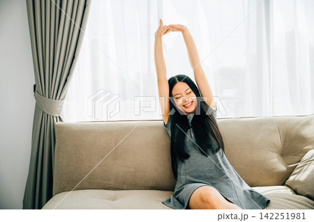 Smiling woman in luxury living room raises arms stretches after sitting Smiling woman in luxury living room raises arms stretches after sitting 142251981