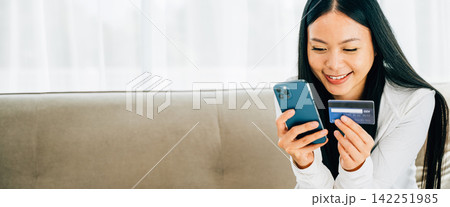 Smiling woman holds smartphone and credit card shops online on sofa Smiling woman holds smartphone and credit card shops online on sofa 142251985