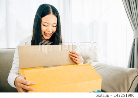 Happy woman in the living room unpacks a cardboard box from online shopping Happy woman in the living room unpacks a cardboard box from online shopping 142251990