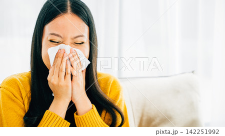 Asian woman blowing her nose holding a handkerchief experiencing flu symptoms at home 142251992
