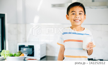 Portrait of smiling Asian little boy in kitchen holding milk. Cute son enjoys drink, radiating joy. Young child savoring calcium-rich liquid, feeling happy at home give me. Portrait of smiling Asian little boy in kitchen holding milk. Cute son enjoys drink, radiating joy. Young child savoring calcium-rich liquid, feeling happy at home give me. 142252012