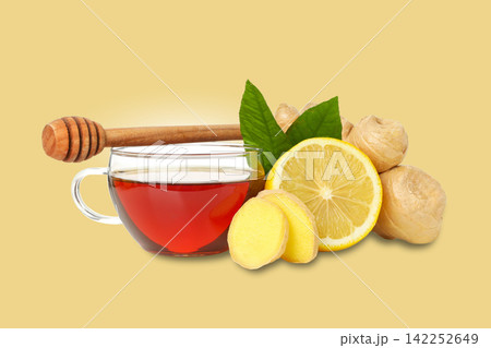 Cup of ginger tea sits beside fresh ginger, lemon slices, and honey 142252649