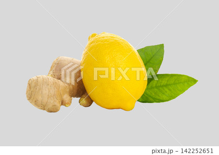 Fresh ginger root sits beside a vibrant lemon with green leaves 142252651