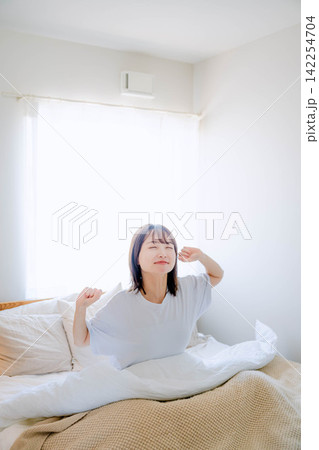寝室のベッドでくつろぐ若い女性 寝室のベッドでくつろぐ若い女性 142254704