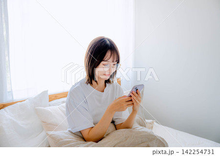 ベッドで携帯電話を使う女性 ベッドで携帯電話を使う女性 142254731